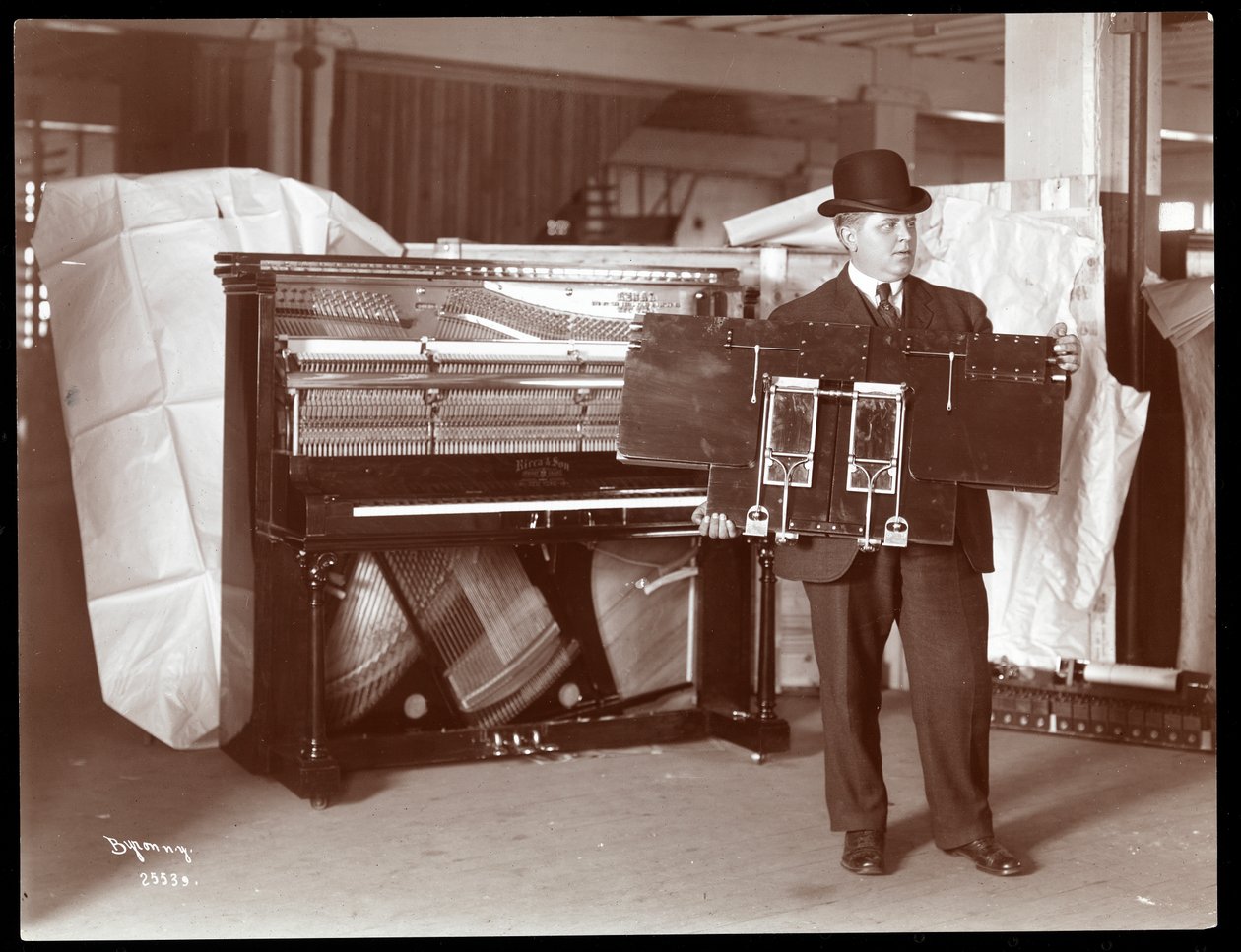 Een piano van Ricca und Son Piano Co. met een man ernaast die een deel van de pianowerken omhoog houdt, 1907 door Byron Company