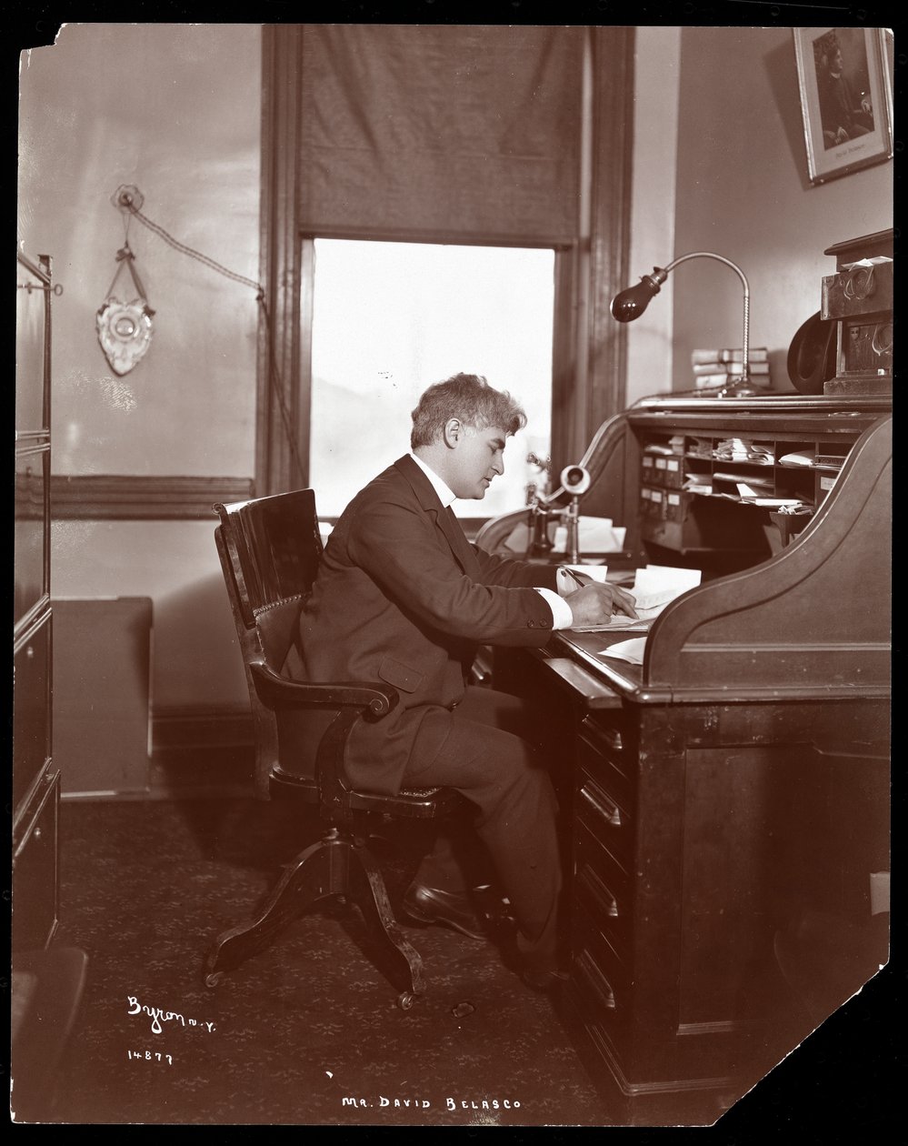 David Belasco schrijft aan een bureau in de kantoren van zijn theater, 1902 door Byron Company