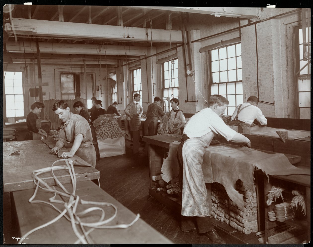 Interieur van mannen en vrouwen die met leer werken bij de New York Leather Belting Co., New York, 1906 door Byron Company