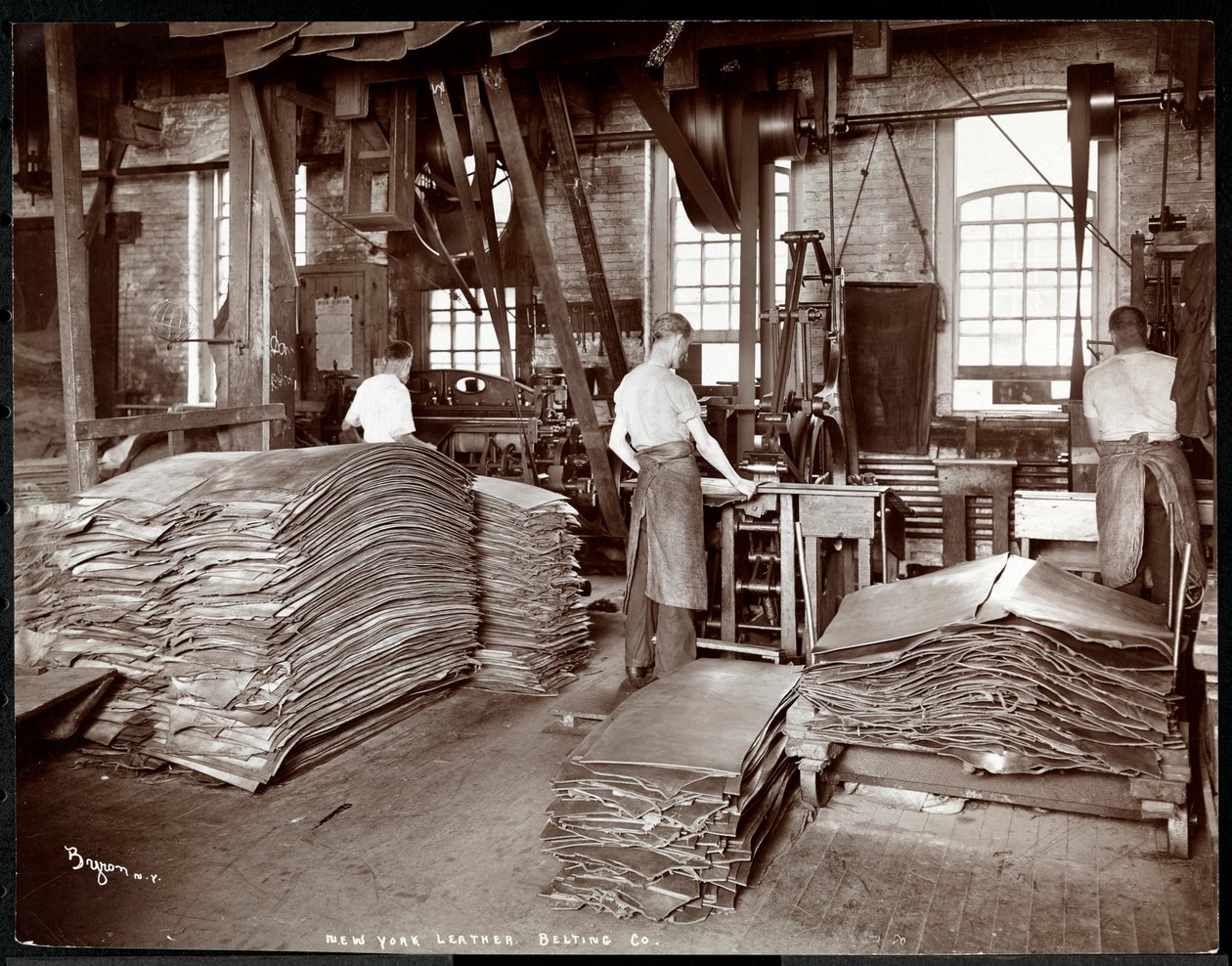 Interieur van drie mannen die met leer en zware apparatuur werken bij de New York Leather Belting Co., New York, 1905 door Byron Company