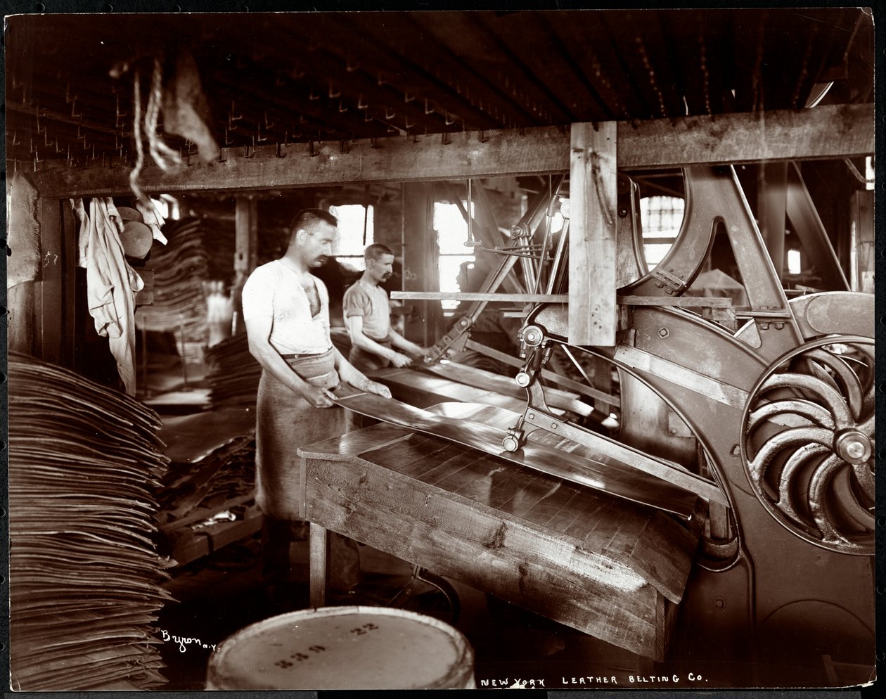 Interieur van twee mannen die werken met leer en zware apparatuur bij de New York Leather Belting Co., New York, 1905 door Byron Company