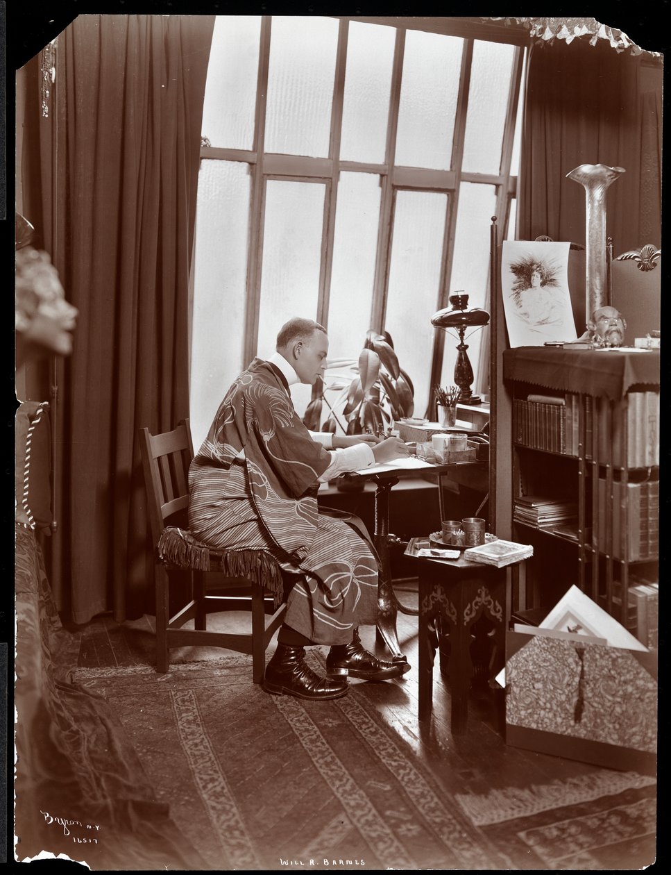 Will R. Barnes in een gewaad, zittend aan zijn bureau in zijn studio, 1903 door Byron Company