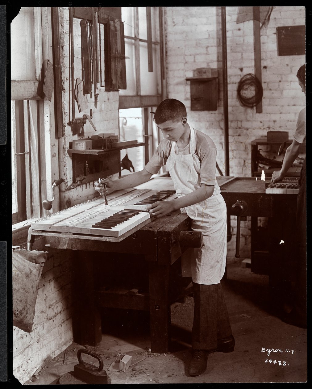 Een jonge man die werkt in de fabriek van Harrington Piano Co., 1907 (zilveren gelatin print) door Byron Company
