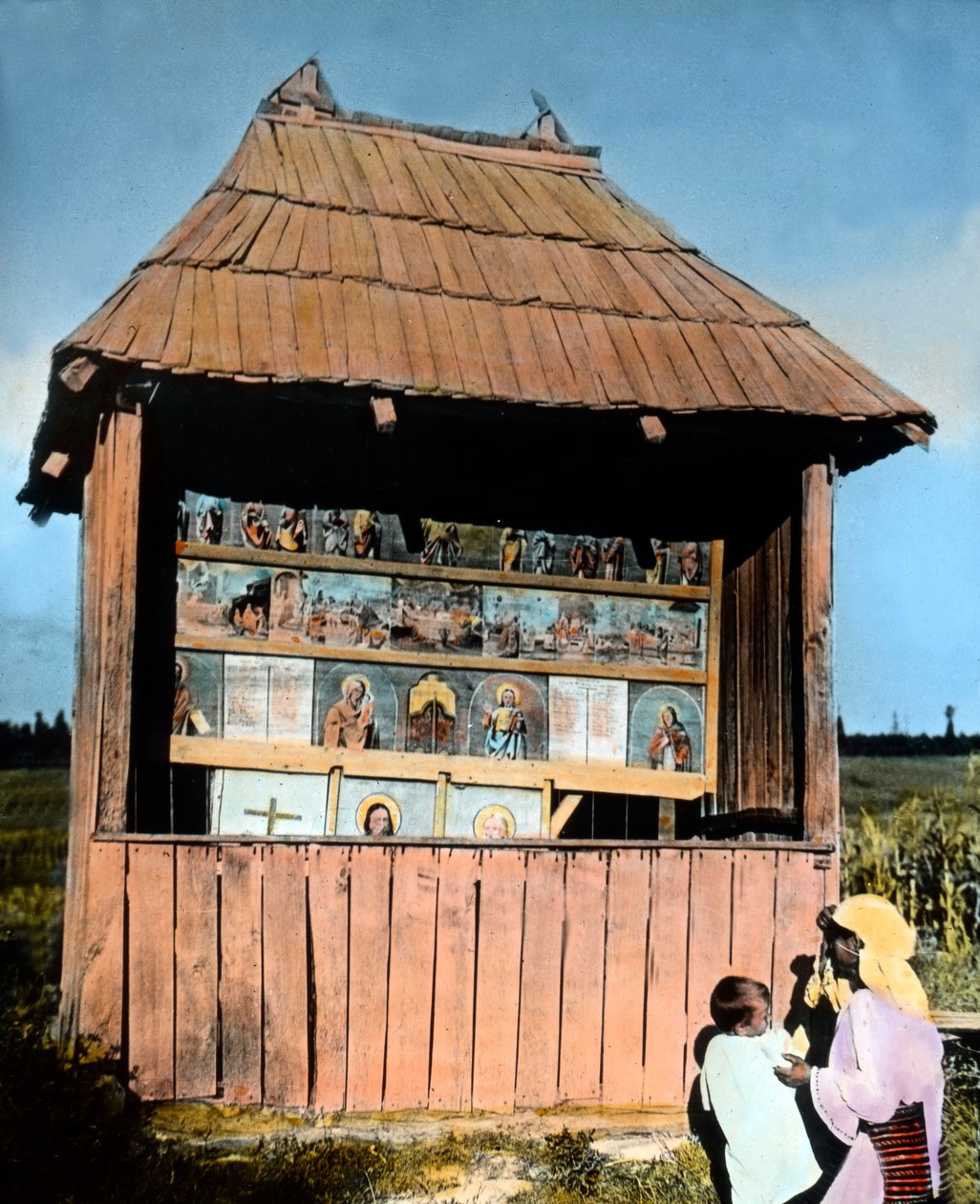 Roemenië, Bukovina, moeder met kind voor een kleine kapel met afbeeldingen van de Heiligen, circa 1920 door Carl Simon