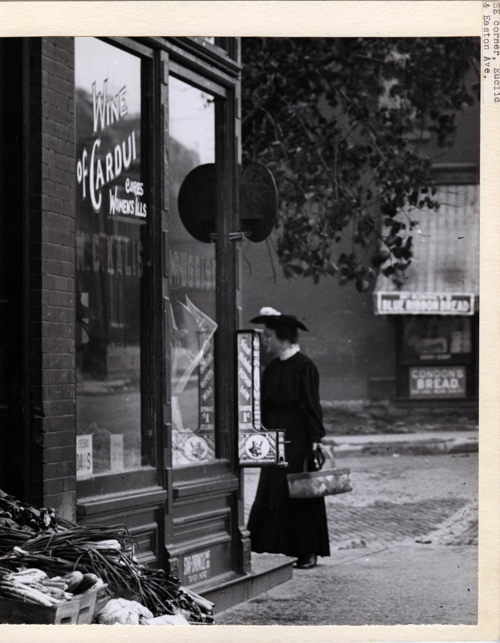 Verticale zwart-witfoto van een vrouw met een mand voor de ingang van de W. C. Kalis apotheek op 4878 Easton Avenue door Charles Clement Holt