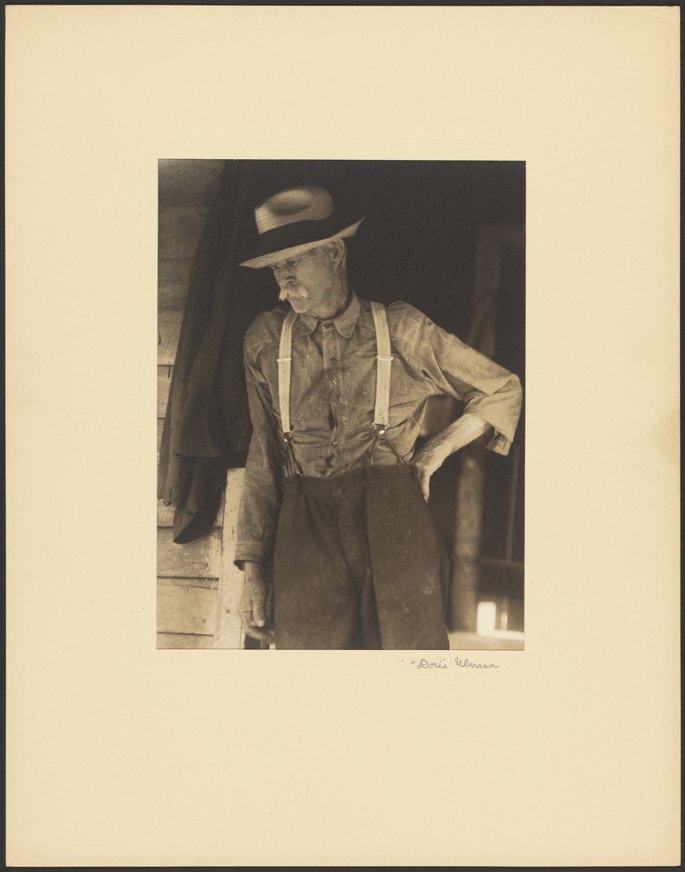 [Besnorde oude man met strohoed en bretels staat in de deuropening]. door Doris Ulmann