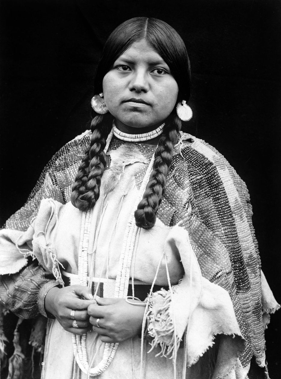 Cayuse vrouw, halflang portret, staand, naar voren gericht, vlechten, schelpschijf oorbellen, schelpkralen choker en schelpkralen om de nek, geborduurde hertenleren jurk met geborduurde riem c. 1910, foto Edward S. Curtis door Edward Sheriff Curtis