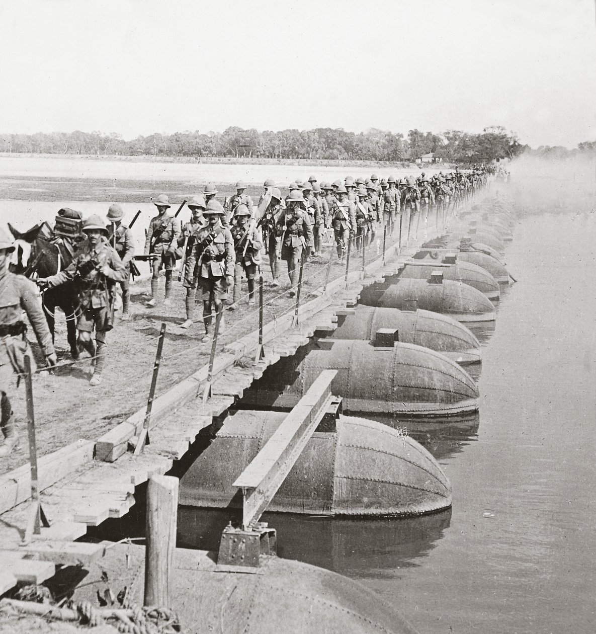 Machinegeweersectie en infanterie steken een overstroomde rivier over via een pontonbrug door English Photographer