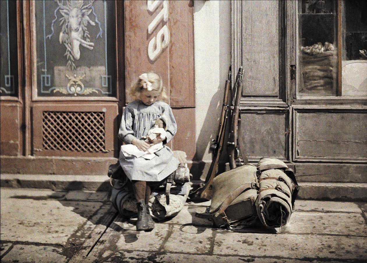 Een klein meisje dat met haar pop speelt; twee geweren en een rugzak liggen naast haar op de grond, Reims, Marne, Frankrijk, 1917 (autochroom) door Fernand Cuville