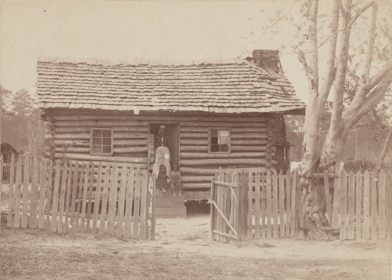 Albuminefoto van een vrouw en twee kinderen voor een blokhut in Georgia door H. S. Clark