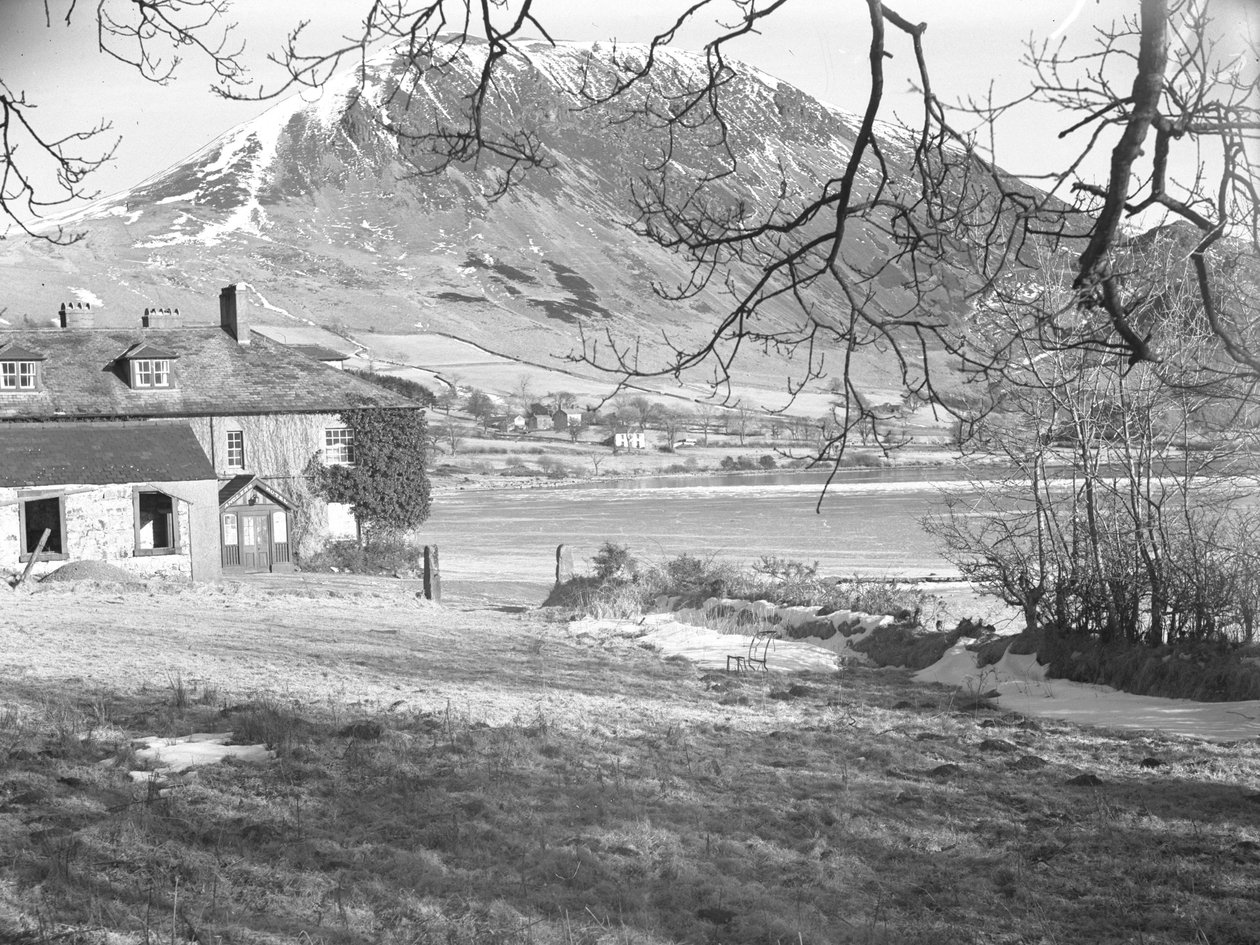 Het Anglers Hotel in Ennerdale met bomen op de voorgrond en bevroren meer en besneeuwde heuvels daarachter door Joseph Hardman