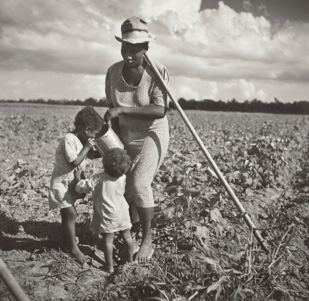 Zwarte vrouw geeft haar kinderen te drinken in het veld waar ze katoen schoffelt op een FSA coöperatief project (Allen Plantation) door Marion Post Wolcott