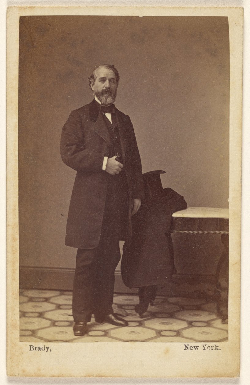 [Een onbekende man met een baard staat rechtop; op een tafel vlakbij liggen een hoge hoed en een jas] door Mathew B. Brady