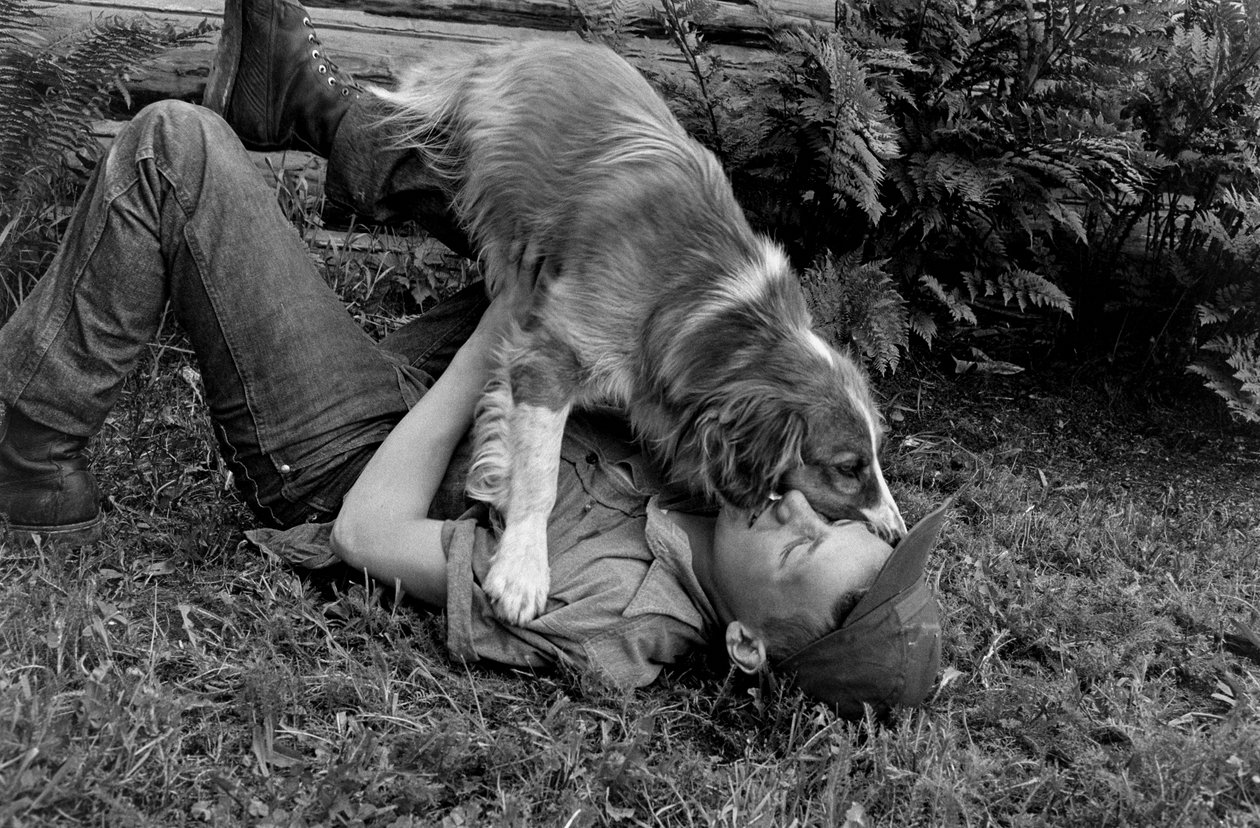 Jonge man speelt met zijn hond buiten hun blokhut in Palmer, Alaska door Ted Spiegel