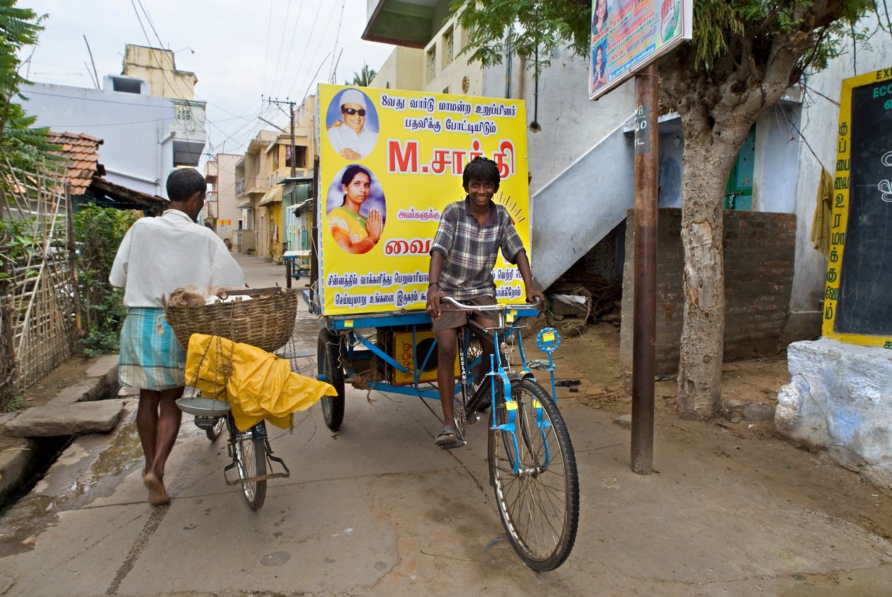 Jongen op posterfiets in smalle straat die campagne voert voor politieke verkiezingen door Unbekannt Unbekannt