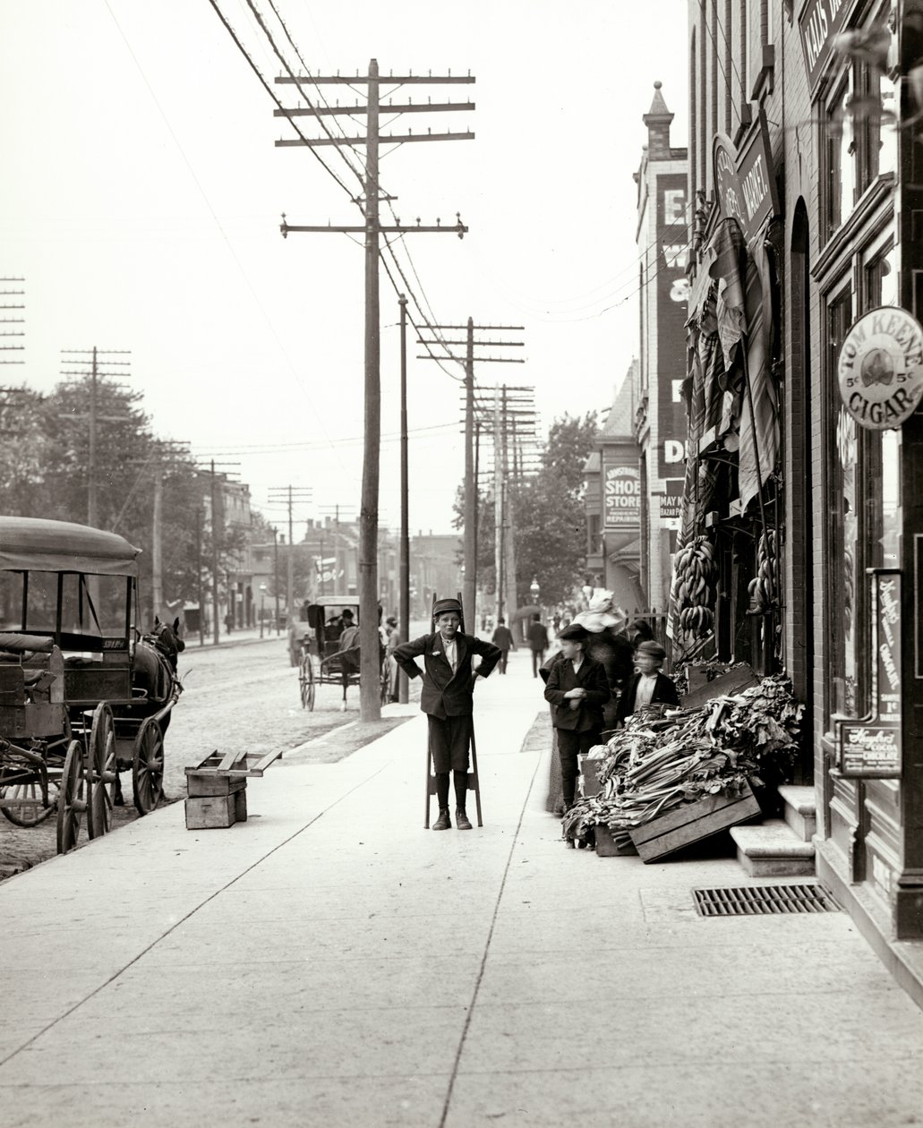 Een jongen met stelten voor de F.J. Voepel Markt op 4874 Easton Avenue, op de zuidoostelijke hoek van Easton en Euclid. Easton werd later bekend als Dr. Martin Luther King Drive door Unknown
