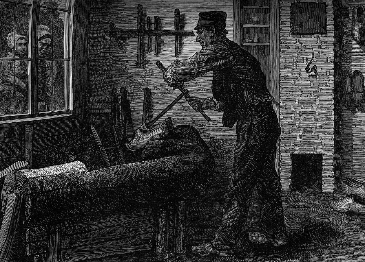 Een klompenmaker aan het werk in zijn werkplaats in België. Gravure in het tijdschrift 