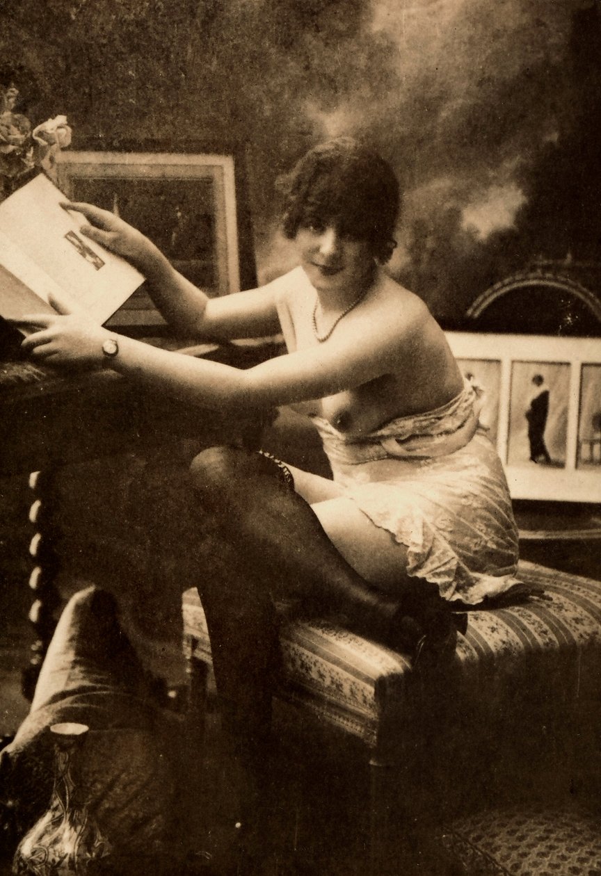 Portret van een jonge vrouw in intieme kleding, zittend aan een tafel met een boek door Unknown photographer