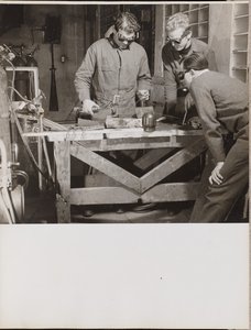 [Drie mannen met veiligheidsbrillen lassen een stuk metaal op een tafel]. door Arnold Eagle