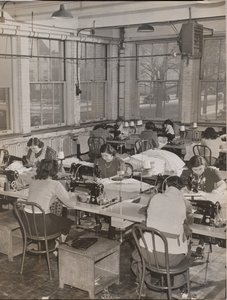 [Vrouwen aan bureaus werken aan naaimachines].