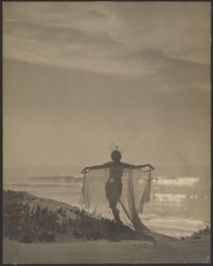 [Achteraanzicht van een danseres die een donker kostuum draagt op het strand].