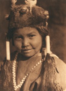 Close-up van een Amerikaanse Indiaanse jongen van de Klamath stam of dorp. Hij draagt een bontmuts met aangebrachte eikels en veren en draagt zijn haar in twee staarten door Edward Sheriff Curtis