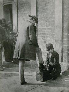 Een jonge schoenpoetser die de schoenen van een man op straat poetst