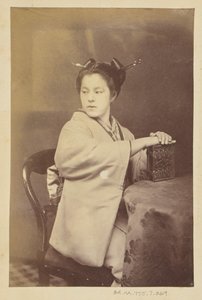 [Zittende Japanse vrouw die een cartes-de-visite album vasthoudt aan een tafel]. door Felice Beato
