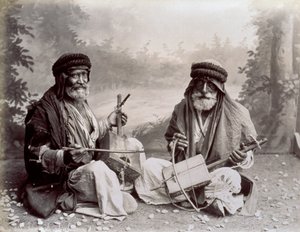 Portret van twee Arabische muzikanten in eenvoudige etnische kleding. De oudere mannen poseren in de studio, zittend op de grond. Achter hen is een achtergrond van een boslandschap door Félix Bonfils