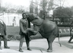 Een jonge Afrikaanse Pygmee-olifant omhelst haar Afrikaanse trainer, terwijl de verzorger toekijkt, London Zoo, juli 1925 door Frederick William Bond