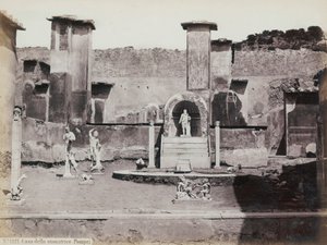 Gedeeltelijk uitzicht op de verhoogde tuin van het Huis van Marcus Lucretius in Pompeii, versierd met marmeren beelden en hermen. In het midden een fontein met een nis. Op de achtergrond fragmenten van muurschilderingen