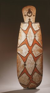 Ovale Asmat schild, gesneden in reliëf met gestileerde figuren, een masker bovenaan