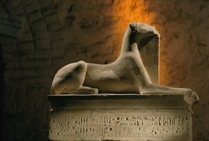 Kalkstenen beeld van de jakhalsgod Anubis geknield op een basis in de vorm van een sarcofaag, 2002