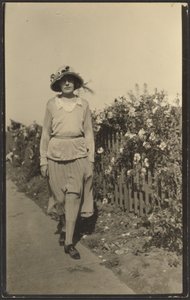 [Vrouw loopt langs hek met bloemen].