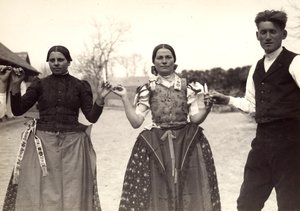 Twee dames en een man in Hongaarse traditionele kleding houden elkaars handen vast in een dans, met kaarsen in hun handen door Rudolf Balogh