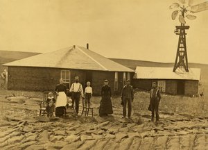 Familie van kolonisten, buiten hun zodenhuis met een windmolen op het dak van het aangrenzende gebouw in Custer County, Nebraska, ca. 1885 door Solomon D. Butcher