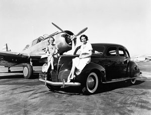 Californië: 1939 Twee Vrouwen Zitten op de Spatborden van een 1939 Lincoln Zephyr Sedan op een Vliegveld met een Eenmotorig Vliegtuig Geparkeerd Achter Hen (zw/w foto) door Unbekannt