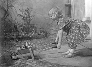 Klein meisje speelt met een kruiwagen. Fotografie rond 1931 door Unbekannt