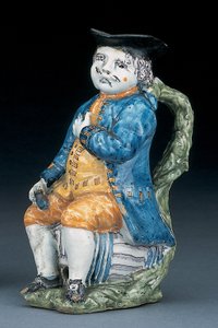 Toby-kruik met bleek mangaan gezicht en handen, houdend een lege bolvormige buffkleurige kruik in gewassen blauwe jas en broek, en groene vest, ca. 1800