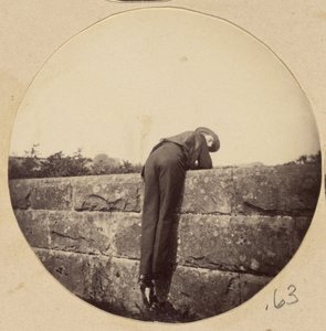 [Man met hoed gebogen over een stenen muur]. door Unknown artist