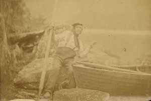 [Man poseert naast roeiboot].