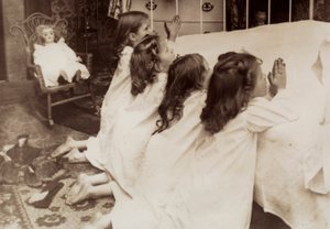 Vier kleine meisjes knielen aan de zijkant van een bed terwijl ze hun avondgebed zeggen