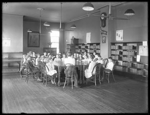 Kinderen luisteren naar een vrouw in de leeszaal van een niet-geïdentificeerde vestiging van de Queens Borough Public Library, c.1910