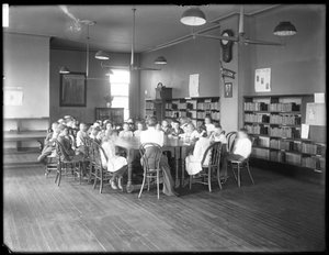 Kinderen luisteren naar een vrouw in de leeszaal van een niet-geïdentificeerde vestiging van de Queens Borough Public Library, ca. 1910