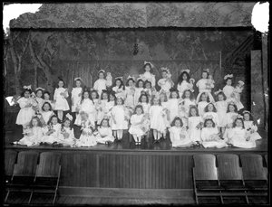 Groep kleine meisjes geposeerd op een klein podium met poppen, waarschijnlijk het Rooms-Katholieke Weeshuis, Kingsbridge, Bronx, ca. 1911