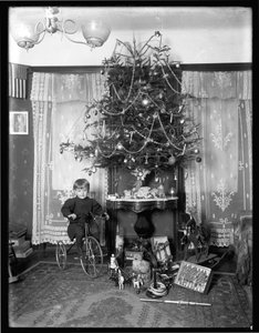 Seymour jongen poseert zittend op driewieler naast kerstboom in salon, Kerstmis 1912 door William Davis Hassler