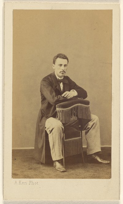 [Man met snor, zittend, met voorkant naar achterkant van stoel met franje]. door Alexandre Ken