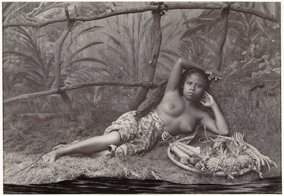 Portret van een onbekende Indonesische halfnaakte vrouw, liggend met een fruitmand in een decor door Anonymous