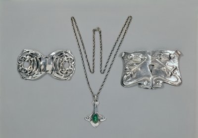 Zilveren sieraden ontworpen voor Liberty. Van links naar rechts: Taille gesp met verstrengeld Keltisch ontwerp, 1904. Hanger en ketting met cabochon geslepen chrysopraas. Taille gesp met repoussé ontwerp op gehamerd door Archibald Knox