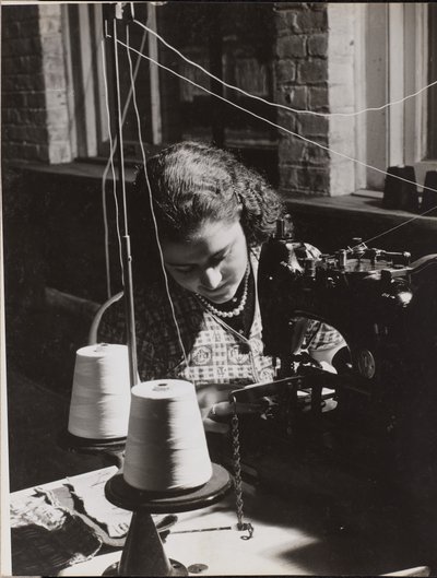 [Vrouw gebruikt een naaimachine met twee spoelen wit garen]. door Arnold Eagle